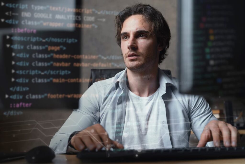 A man works at a computer, program code is in the foreground
