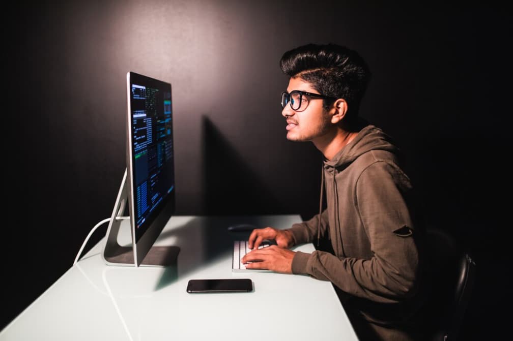 A young man coding on a computer in a dark room