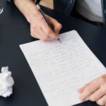 A man writes a letter in pencil on paper
